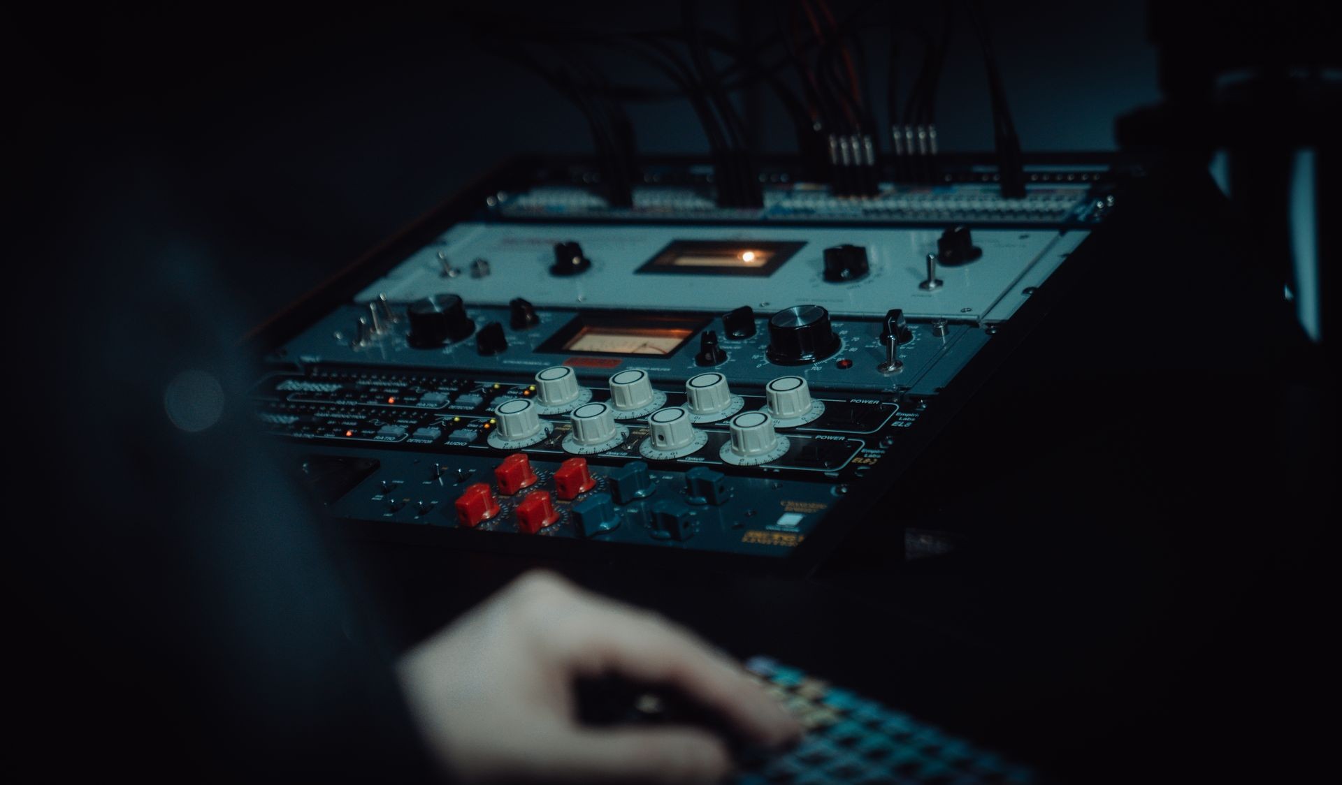 Close-up of a hand operating an audio mixing console with dials and switches.